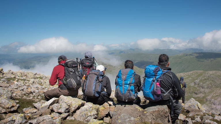 A group of five walkers rest above the clouds at the summit of Great End, Wasdale, Cumbria